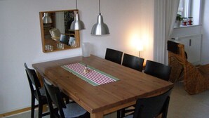 Ein Essbereich mit Holztisch, sechs Stühlen, einem Spiegel und Pendelleuchten.