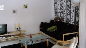 Ein Wohnzimmer mit einem schwarzen Sofa, einem Glastisch, einem Fernseher und einer Lampe.