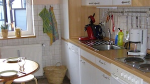Eine Küche mit weißen Schränken, einem Herd, einer Spüle und einem Fenster mit Vorhängen.