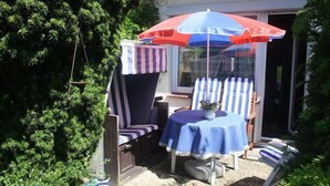 A patio with a striped chair and table, an umbrella, and a window. - Middle row house near the beach, quiet location but in the middle of life (Butjadingen)