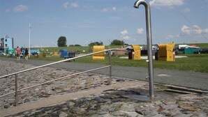A rocky waterfront with metal railings and yellow structures in the background. - Middle row house near the beach, quiet location but in the middle of life (Butjadingen)