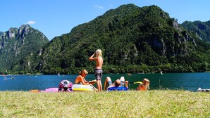 A group of people relaxing on a grassy area with a lake and mountains in the background. - Directly from the owner (Tre Capitelli)