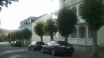 Un carrer amb cotxes aparcats i un edifici de façana blanca amb balcons.