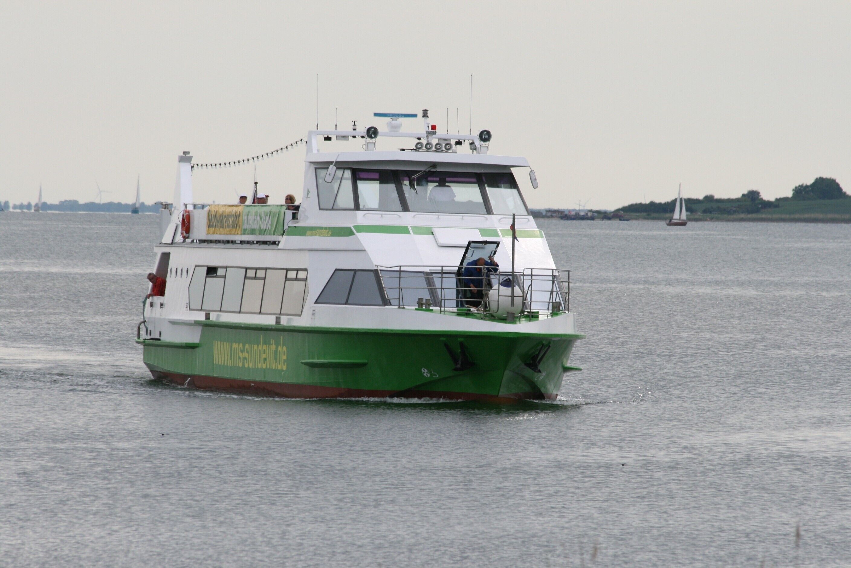Un ferry blanco y verde con una dirección web en su costado, navegando sobre el agua.