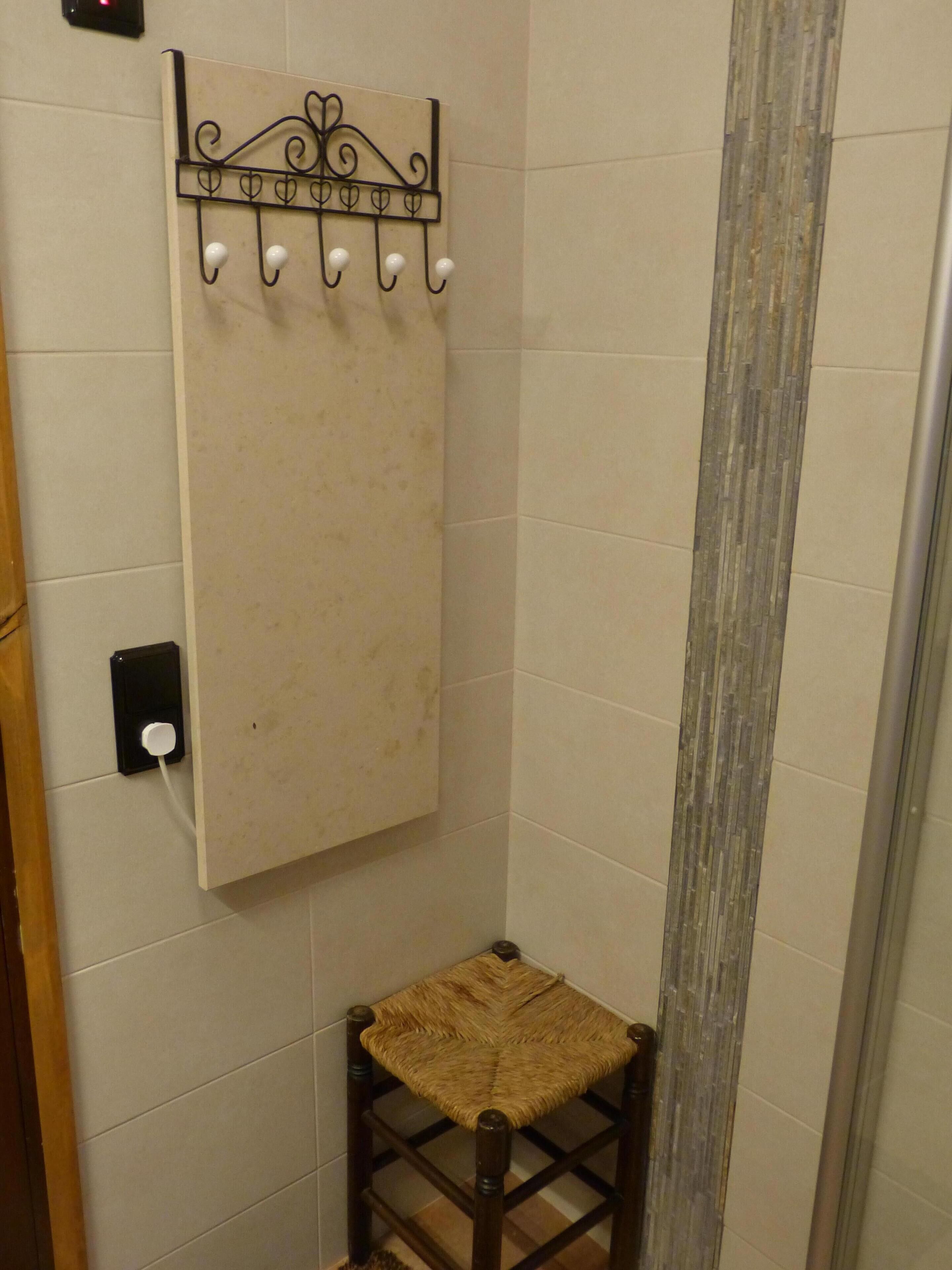 A bathroom with a towel rack, a small stool, and a wall-mounted switch.