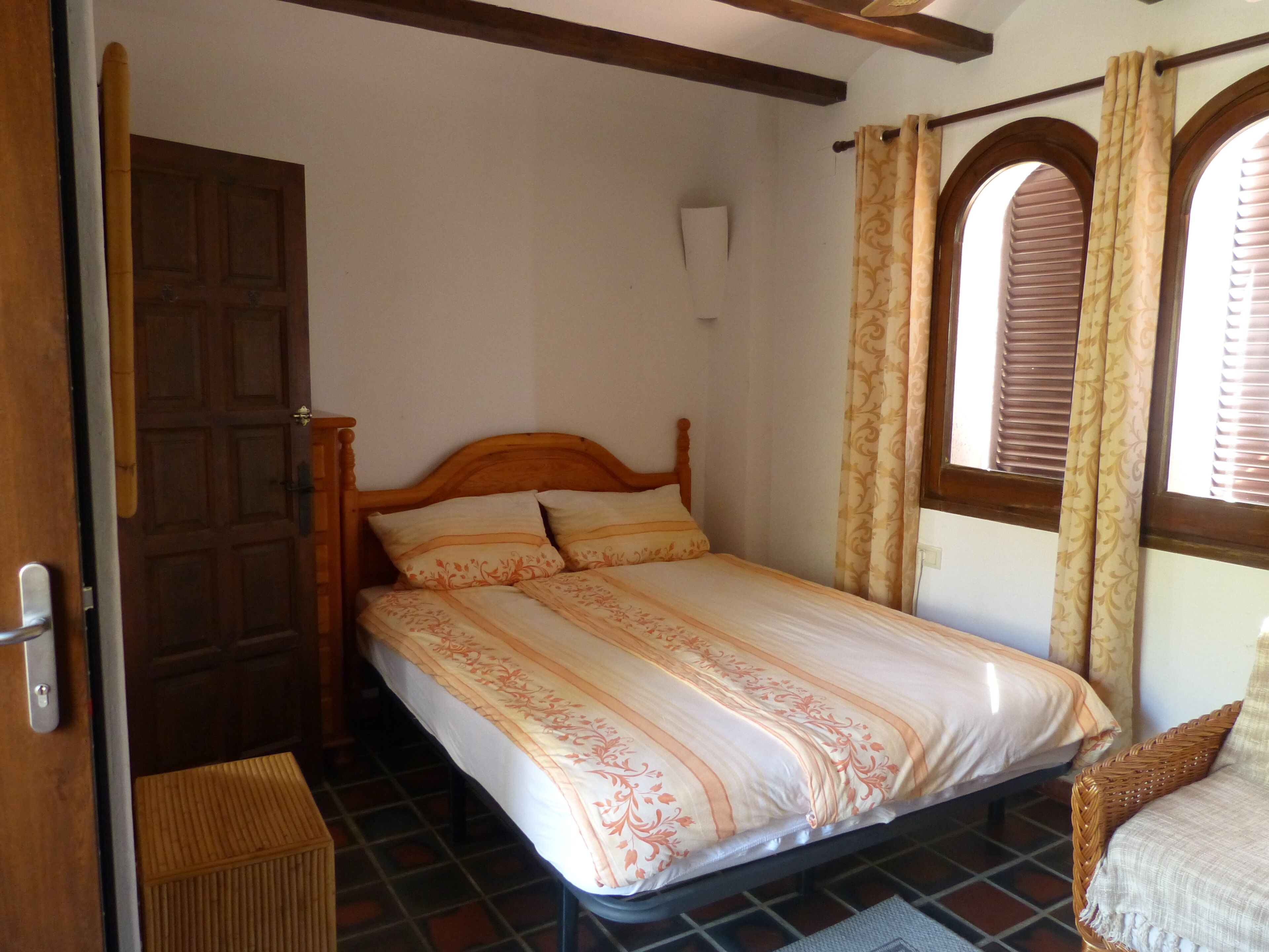 A single bed with a wooden headboard, a patterned bedspread, and a window with curtains.