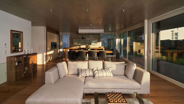 A modern living room with a large sectional sofa, a chessboard, and a kitchen in the background. - LOFT Rebhalde in Nonnenhorn on Lake Constance offers relaxation and comfort at the same time (Nonnenhorn)