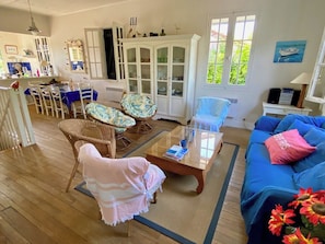 A living room with a blue sofa, wicker chairs, a glass coffee table, and a cabinet with glass doors. - Wonderful villa with idyllic garden A0338 (Lège-Cap-Ferret)