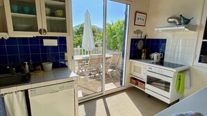 A compact kitchen with a built-in dishwasher, a microwave, and a stove. There is a sliding glass door leading to an outdoor patio with a table and chairs. - Fantastic house with idyllic garden in the heart of Cap Ferret, very central (Lège-Cap-Ferret)