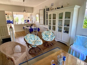 A spacious room with a dining area, two wicker chairs with patterned cushions, a cabinet with glass doors, and a blue chair. - Wonderful villa with idyllic garden A0338 (Lège-Cap-Ferret)