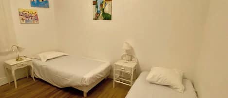 Een kamer met twee bedden, een nachtkastje, een lamp en twee aan de muur bevestigde schilderijen.