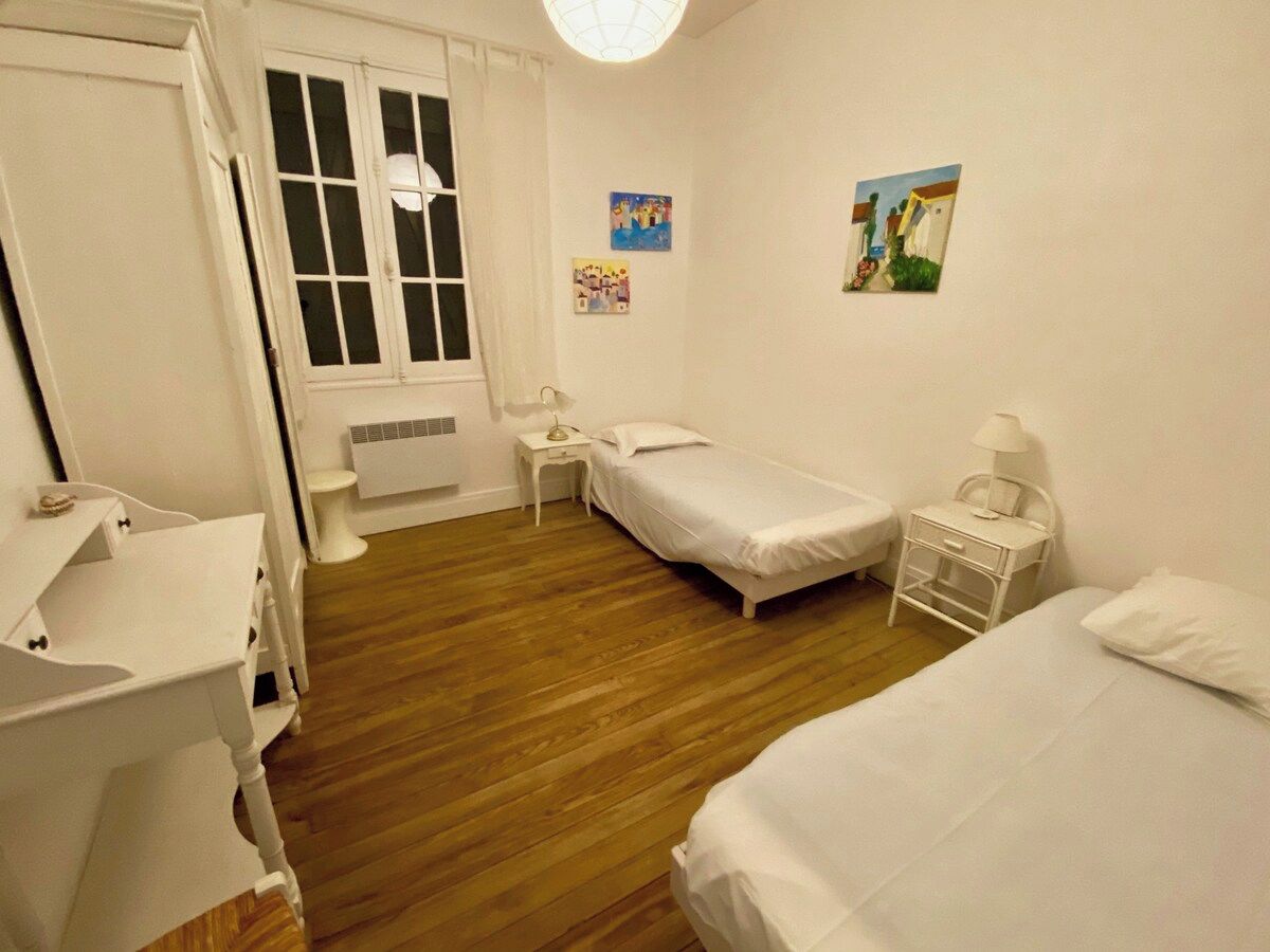 A bedroom with two single beds, a bedside table, a nightstand, a small table with a lamp, and a wall-mounted picture.