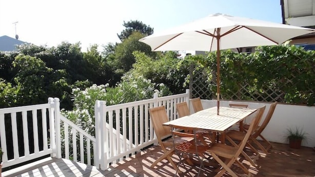 An outdoor patio with a wooden table and chairs, a white fence, and a large umbrella. - Fantastic house with idyllic garden in the heart of Cap Ferret, very central (Lège-Cap-Ferret)