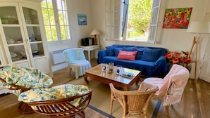 A cozy living room with a blue sofa, wicker chairs, a coffee table, and a dining table. - Fantastic house with idyllic garden in the heart of Cap Ferret, very central (Lège-Cap-Ferret)