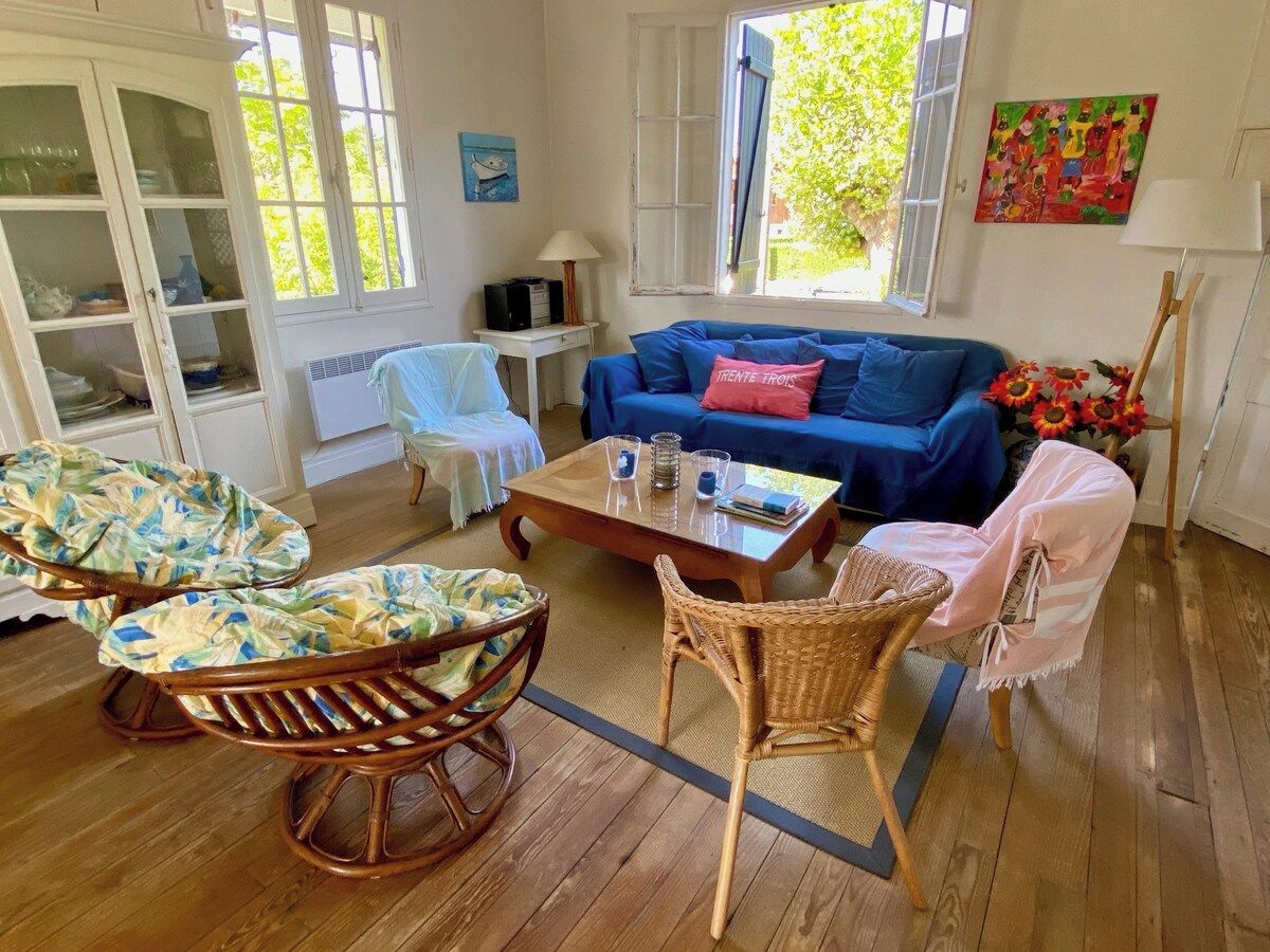 Ein Zimmer mit einem blauen Sofa, Korbstühlen, einem Holztisch und Blick auf Grün.