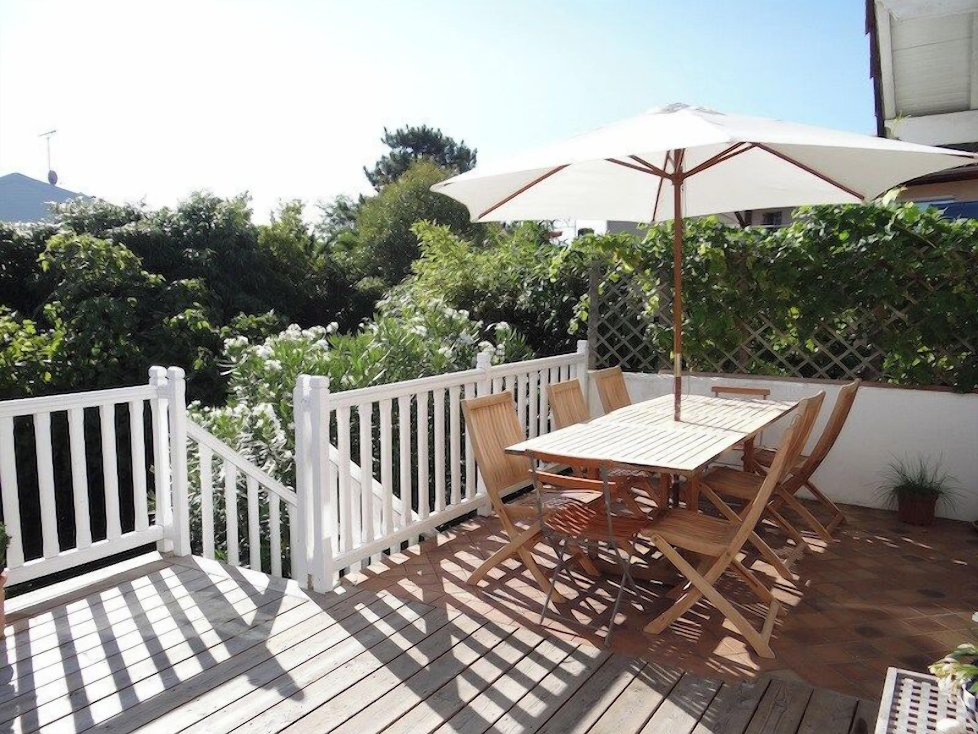 Un patio esterno con tavolo e sedie di legno, una recinzione bianca e un ombrellone grande.