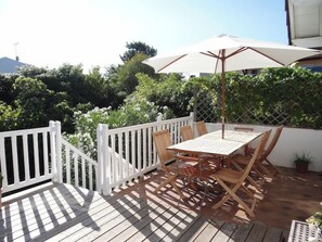An outdoor patio with a wooden table and chairs, a white fence, and a large umbrella. - Wonderful villa with idyllic garden A0338 (Lège-Cap-Ferret)