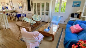 A cozy living room with a blue sofa, wicker chairs, a coffee table, and a dining area with a table and chairs. - Fantastic house with idyllic garden in the heart of Cap Ferret, very central (Lège-Cap-Ferret)