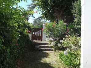 A pathway leading to a gated entrance surrounded by lush greenery and flowering plants. - Wonderful villa with idyllic garden A0338 (Lège-Cap-Ferret)
