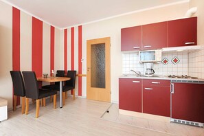 Cozinha compacta com micro-ondas, fogão e armários vermelhos. Possui um espaço de refeições com mesa e cadeiras.