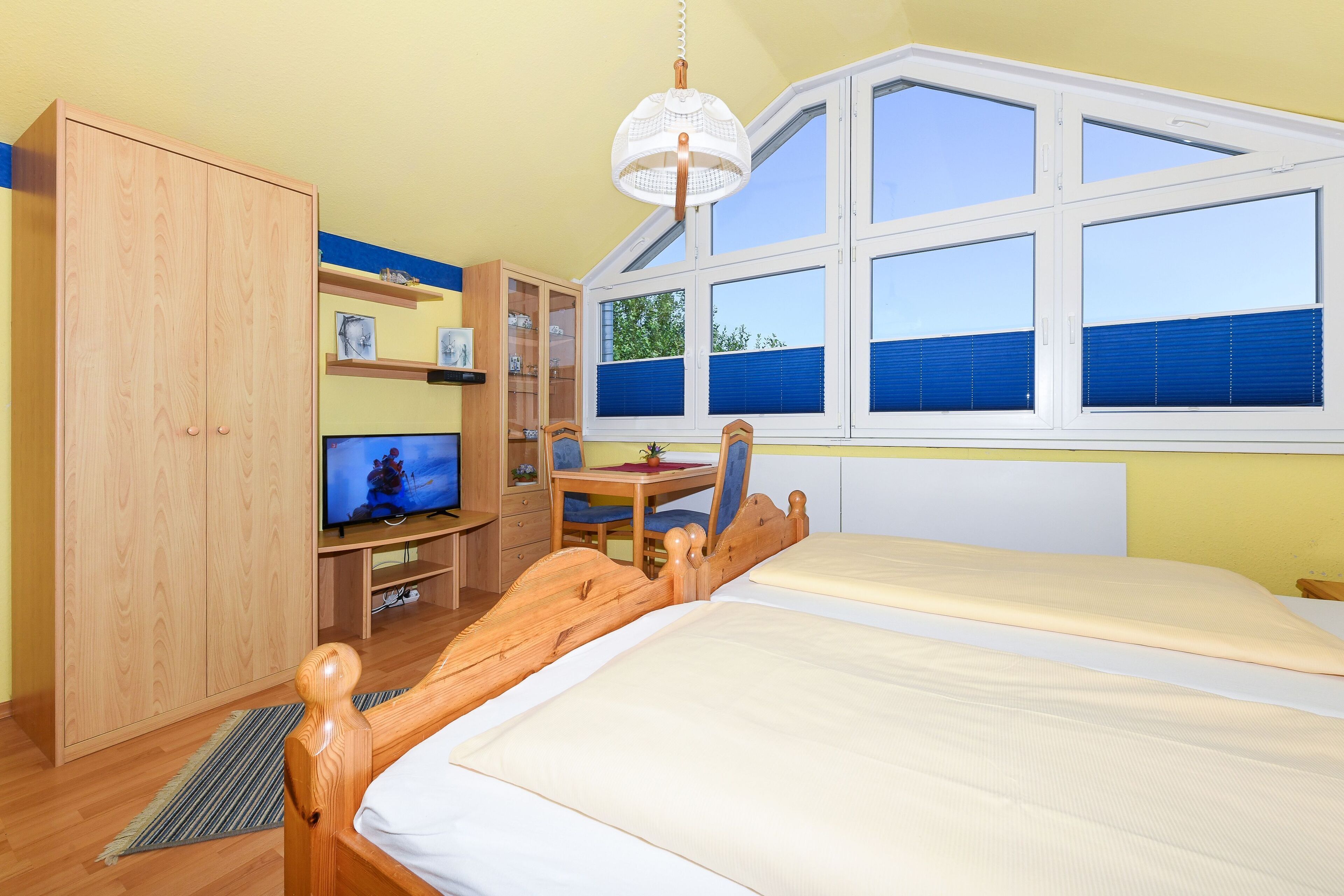 Een slaapkamer met een bed, een houten garderobe, een televisie en een raam met jaloezieën.