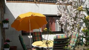 An outdoor patio with a round table and chairs, an orange umbrella, and potted plants. - Large, comfortable apartment in a quiet outskirts. (Sinsheim)