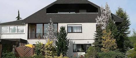 A two-story house with a dark roof, large windows, and a balcony.