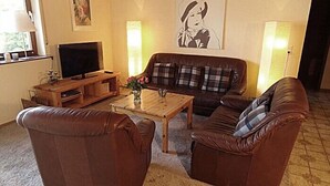A living room with a brown leather sofa, a wooden coffee table, a TV on a wooden stand, and a painting on the wall. - Large, comfortable apartment in a quiet outskirts. (Sinsheim)
