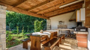 An outdoor kitchen with wooden tables and benches, a stone wall, and a view of greenery. - Summer offer/ Villa ULIKA, near the sea/with private pool/quiet place (Rakalj)