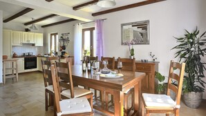 A dining area with wooden furniture, a kitchen in the background, and a large window with curtains. - Summer offer/ Villa ULIKA, near the sea/with private pool/quiet place (Rakalj)