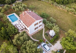 Una casa de dos pisos con piscina, un porche cubierto y un jardín.