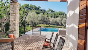 An outdoor patio with a wooden table and chairs, a stone pillar, and a view of a swimming pool and trees. - Summer offer/ Villa ULIKA, near the sea/with private pool/quiet place (Rakalj)