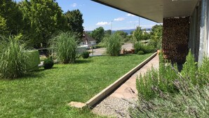 A well-maintained garden with a gravel pathway, various plants, and a building with a stone wall. - FeWo Betz Bodensee in Überlingen (Überlingen)