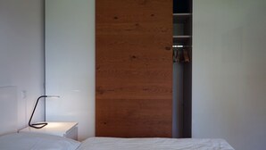 A bedroom with a white bed, a bedside table with a lamp, and a wooden panel wall. - FeWo Betz Bodensee in Überlingen (Überlingen)