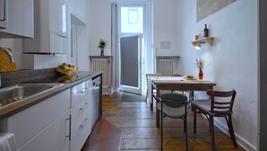 A narrow kitchen with a dining area, wooden flooring, white cabinetry, and a radiator. - Renovated old apartment with shower room, separate eat-in kitchen and washing machine (Berlin)