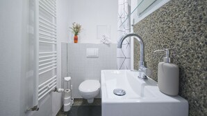 A modern bathroom with a white sink, a toilet, a shower with a glass door, and a towel rack. - Renovated old apartment with shower room, separate eat-in kitchen and washing machine (Berlin)