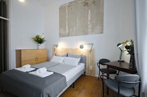 Et moderne hotelværelse med en trægavl, en stor seng med hvide sengetøj, et skrivebord med stol og en lampe monteret på væggen.