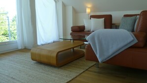 A modern living room with a glass coffee table, a brown sofa, and a white blanket. - Haus Mirabelle: Baltic Sea view through trees close to the beach (5 min walk) (Kalkhorst)