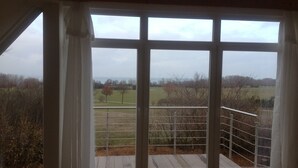 A room with a large window overlooking a rural landscape. - Haus Mirabelle: Baltic Sea view through trees close to the beach (5 min walk) (Kalkhorst)