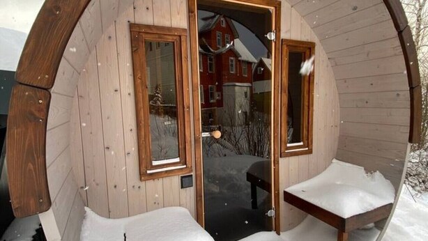 Una estructura de iglú de madera con dos bancos y una puerta, rodeada de nieve.