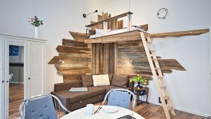 Een gezellige woonkamer met een houten accentmuur, een hoogslaper, een eettafel met stoelen en een kast.