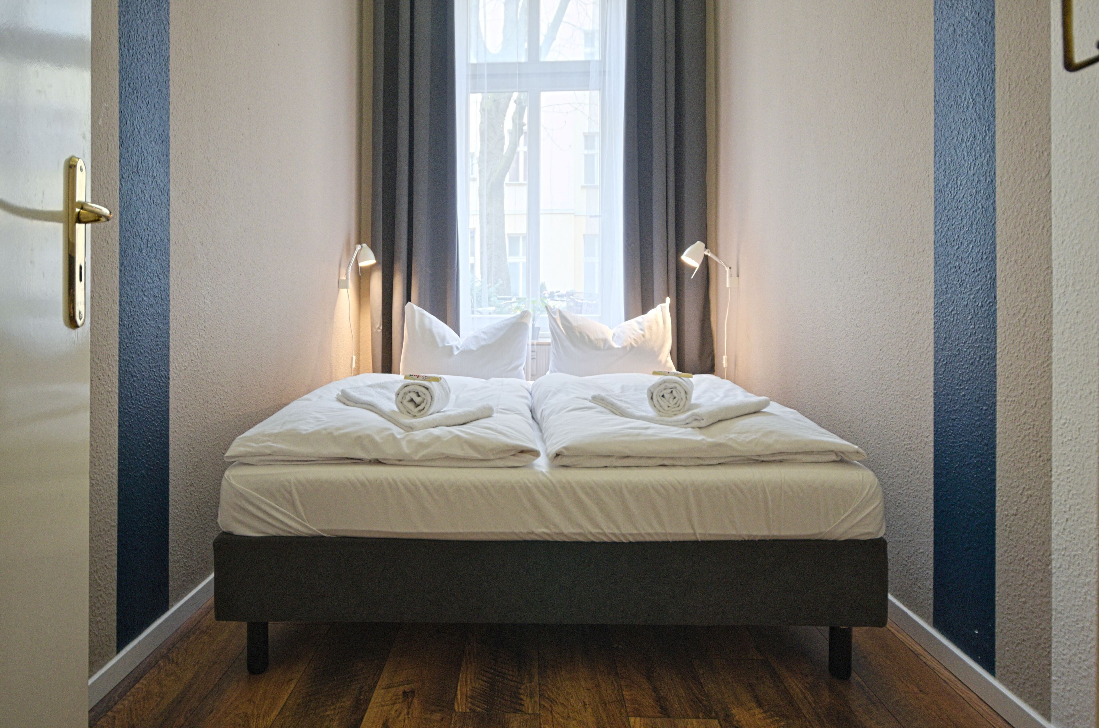 Ein ordentlich bezogenes Bett mit weißen Leinen, einem dunklen Kopfteil und einem Fenster mit Vorhängen.