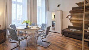Een moderne woonkamer met een ronde eettafel, metalen stoelen, een bank en een houten trap.