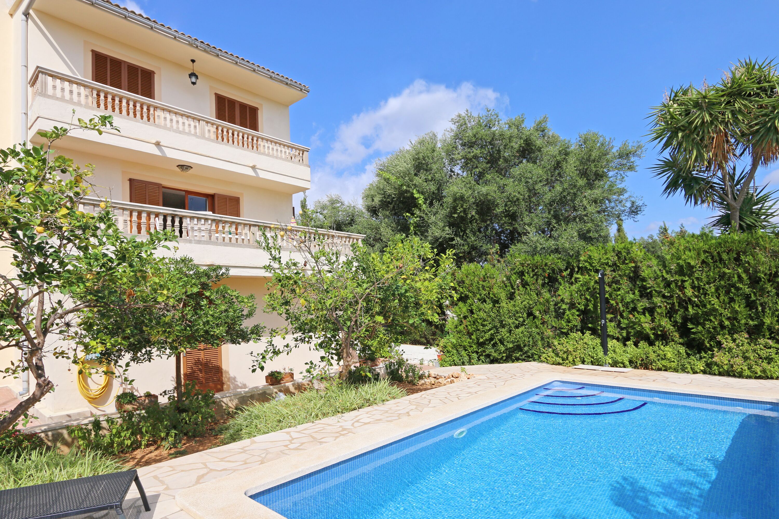 A two-story building with a swimming pool, surrounded by lush greenery and trees.