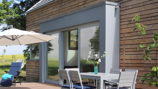 Una casa moderna con fachada de madera, un deck con mesa y sillas, y un paraguas grande.