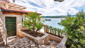 A stone staircase leading to a green door, a small garden with plants, and a view of boats on a lake with hills in the background. - Nice villa direct on sea,surrounded with lot of mediterranean plants,two minutwe (Klek)