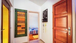 A hallway with a wooden door, a green-framed window, and a bed with a striped bedspread. - Nice villa direct on sea,surrounded with lot of mediterranean plants,two minutwe (Klek)