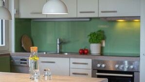A kitchen with white cabinets, a green backsplash, a stainless steel oven, and a bottle with a cork.