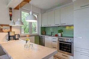 A modern kitchen with white cabinets, a stainless steel oven, and pendant lights. - On the wildly romantic natural beach, enchanting view, cozy with stove, sauna (Schleswig Holstein)