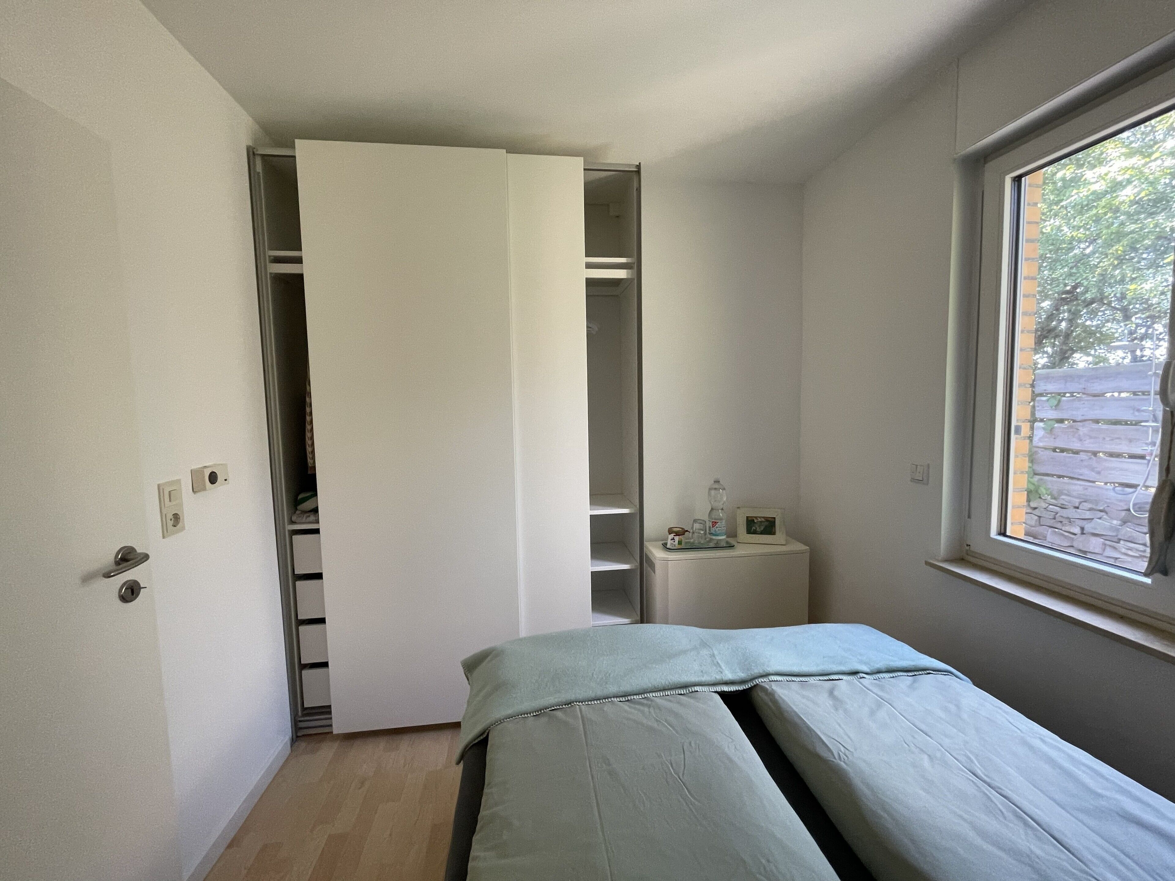 A bedroom with a bed, a window, a bedside table, and a closet.
